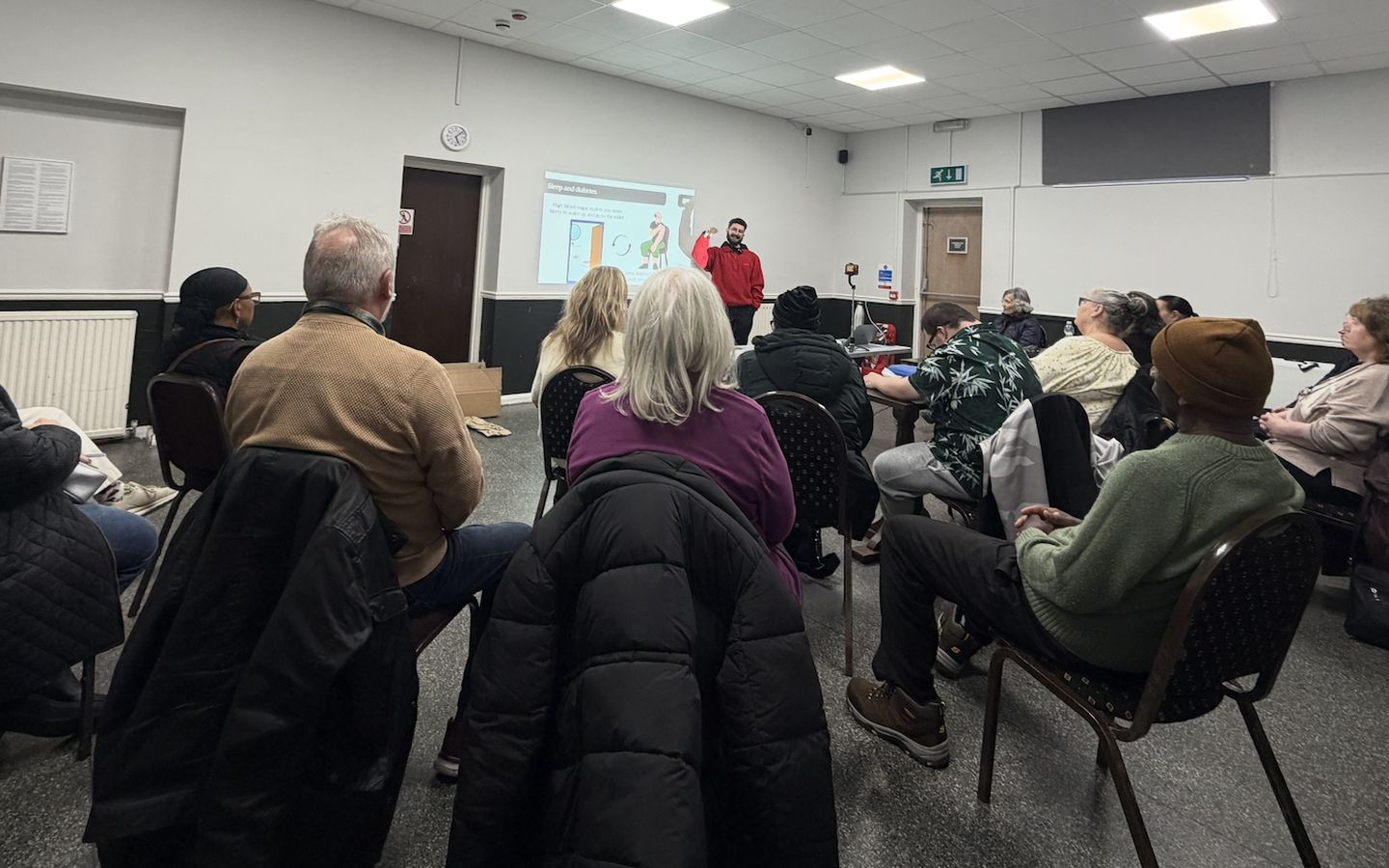 A full room seated for one of Zak's health sessions, with a slide on sleep and diabetes on screen.